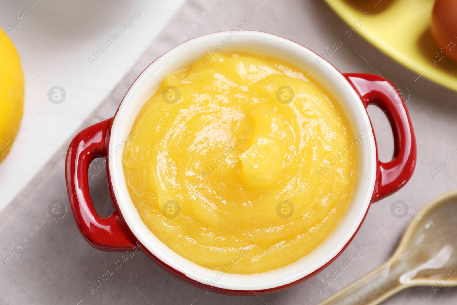 Photo of Delicious lemon curd in bowl and spoon on table, flat lay