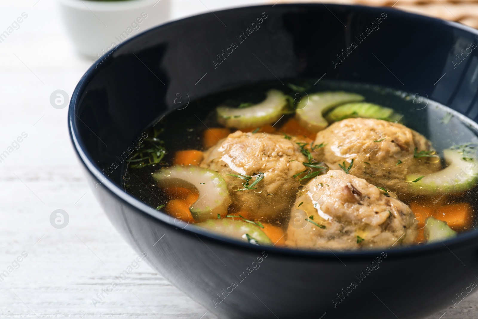 Photo of Bowl of Jewish matzoh balls soup on white wooden table, closeup