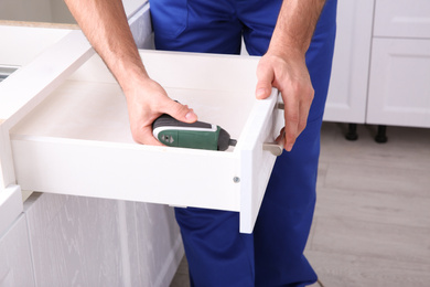 Photo of Worker installing kitchen furniture with electric screwdriver, closeup