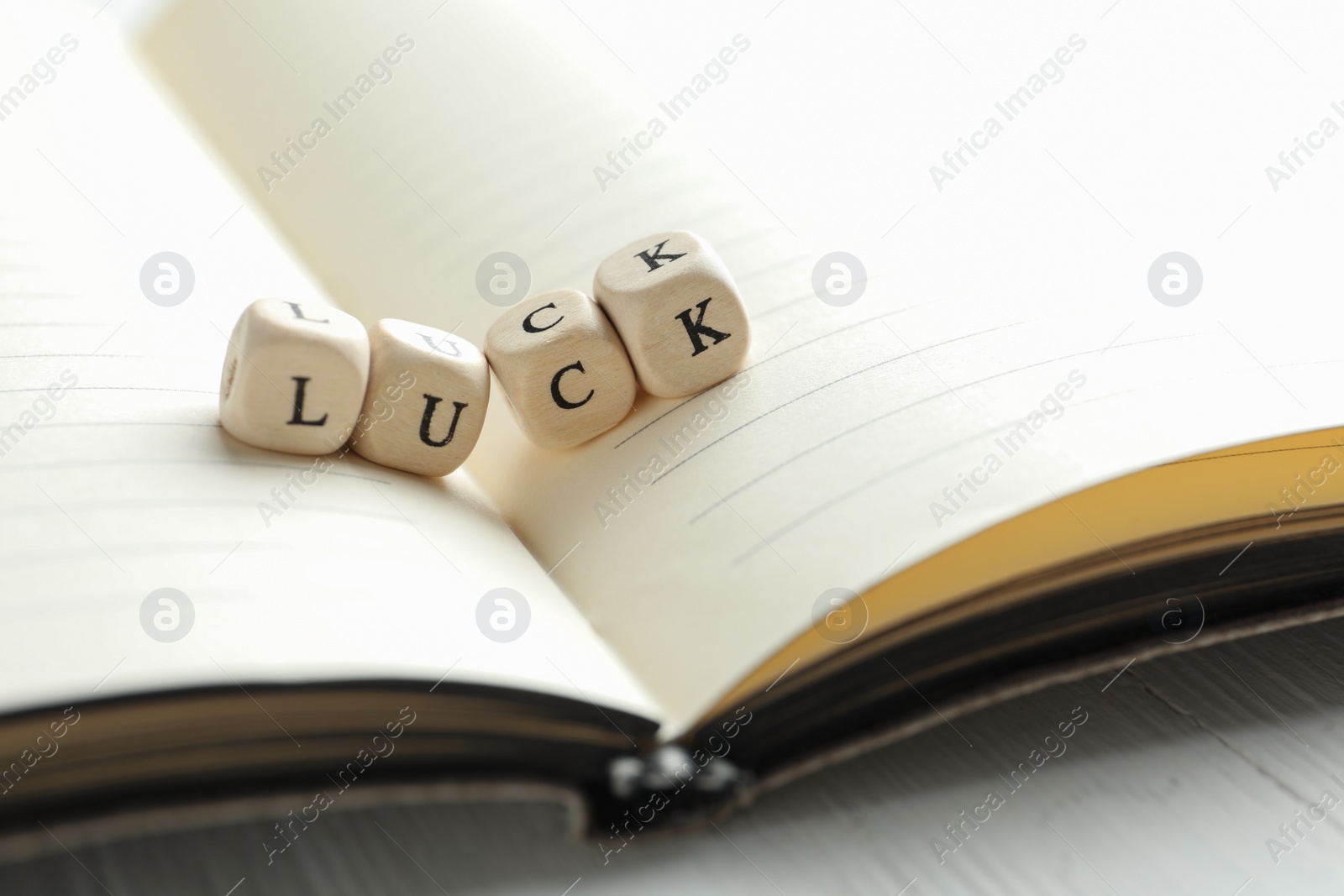 Photo of Word LUCK made with wooden cubes and open notebook on table, closeup