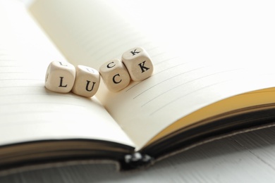 Photo of Word LUCK made with wooden cubes and open notebook on table, closeup