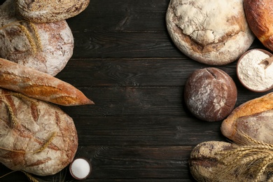 Photo of Different kinds of fresh bread on black wooden table, flat lay. Space for text