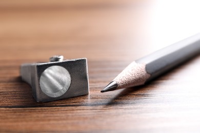 Photo of Metal sharpener and grey pencil on wooden table, closeup