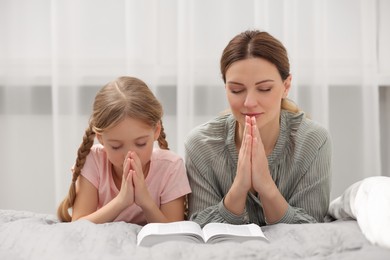 Photo of Girl and her godparent praying over Bible together at home