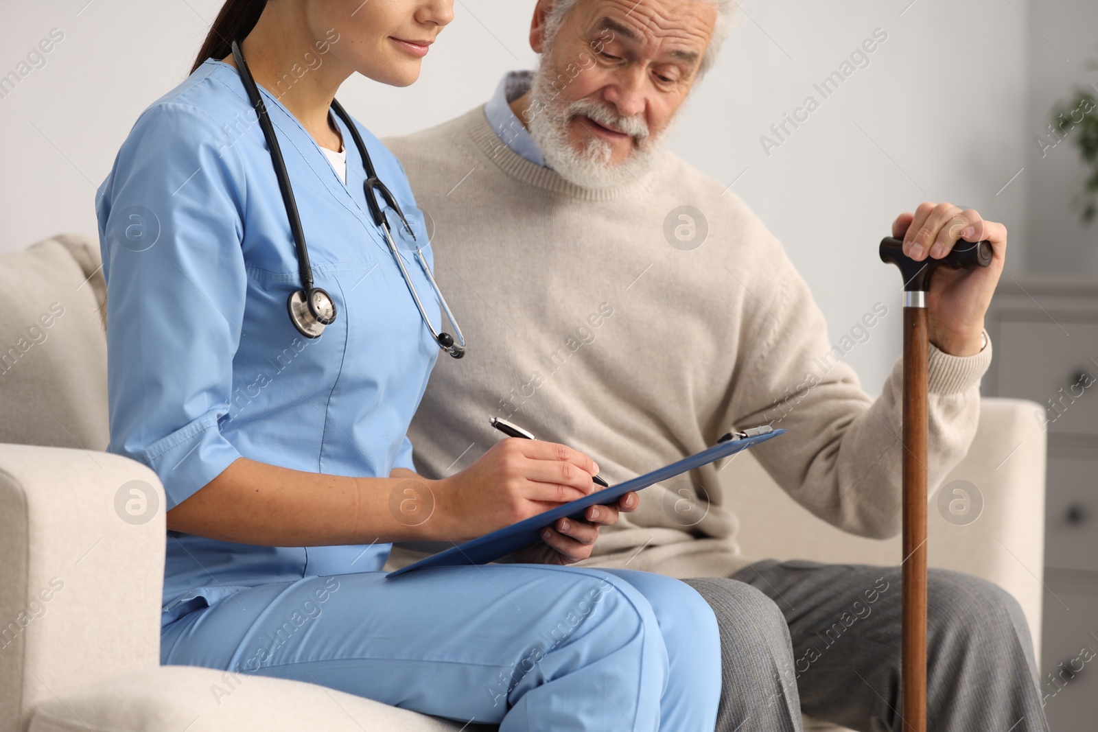 Photo of Nurse with clipboard assisting elderly patient in hospital, closeup