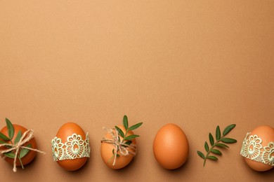 Photo of Festively decorated chicken eggs on brown background, flat lay and space for text. Happy Easter