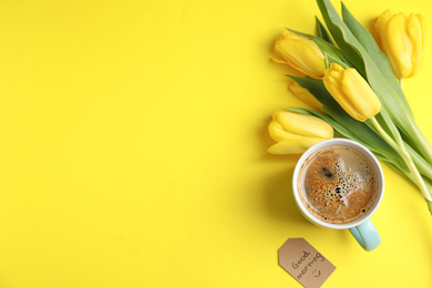 Photo of Aromatic coffee, beautiful flowers and GOOD MORNING wish on yellow background, flat lay. Space for text