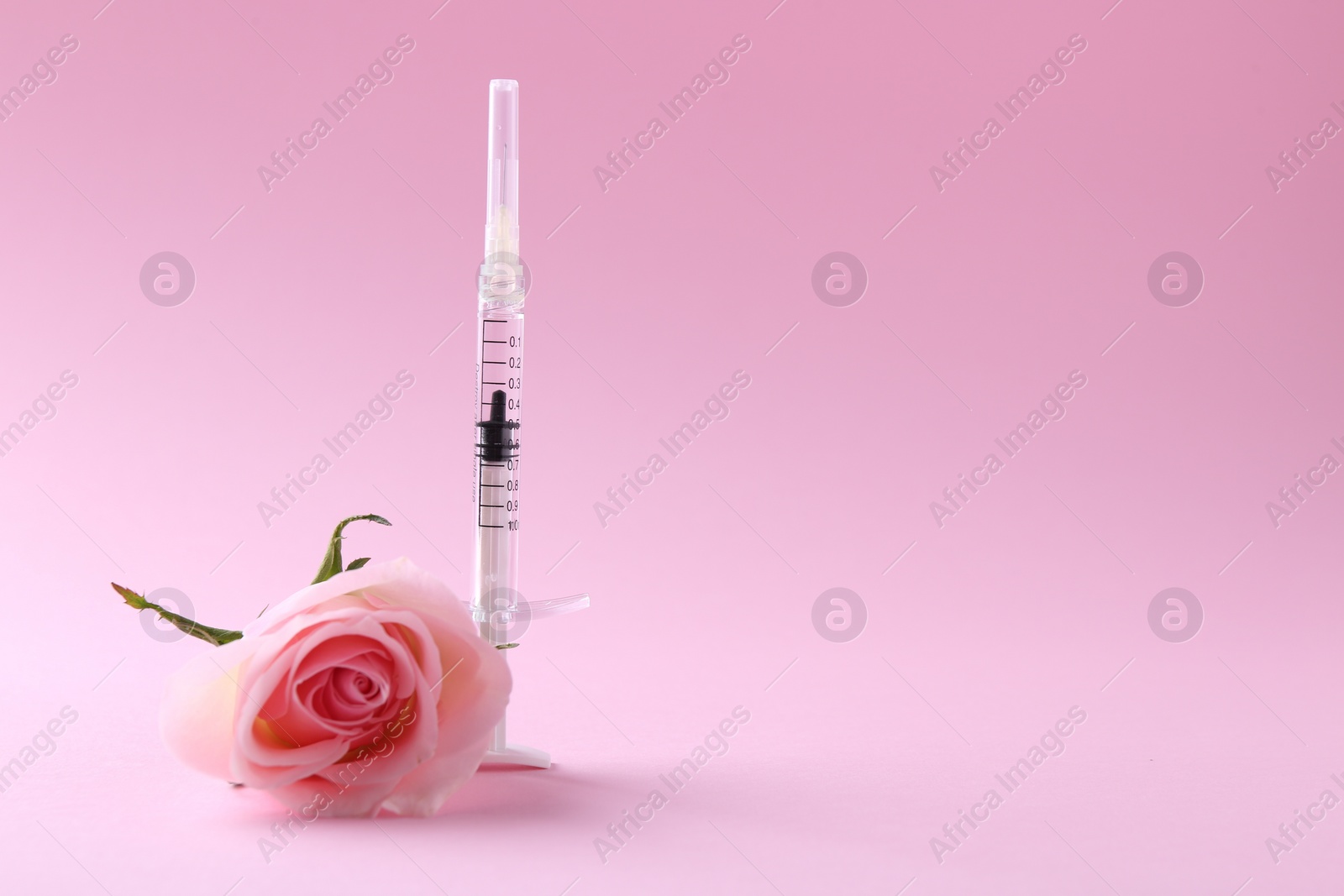 Photo of Cosmetology. Medical syringe and rose flower on pink background, space for text