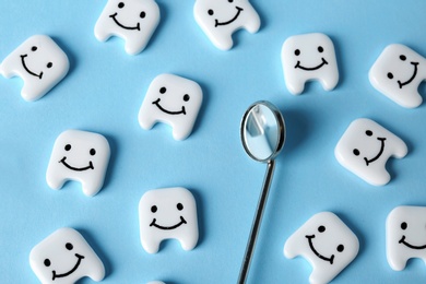 Many small plastic teeth with cute faces and mouth mirror on color background, top view