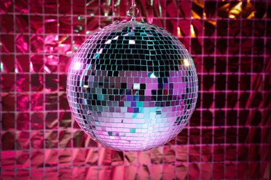 Photo of Shiny disco ball against foil party curtain under pink light