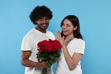 International dating. Handsome man presenting roses to his beloved woman on light blue background