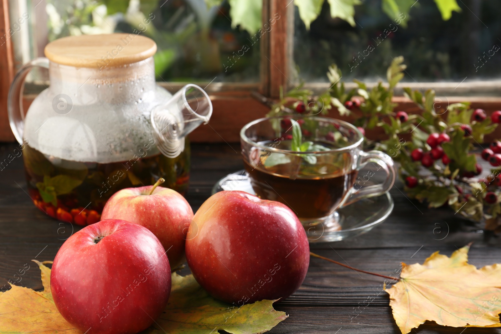 Photo of Hot tea, apples and dry leaves on wooden windowsill. Autumn atmosphere