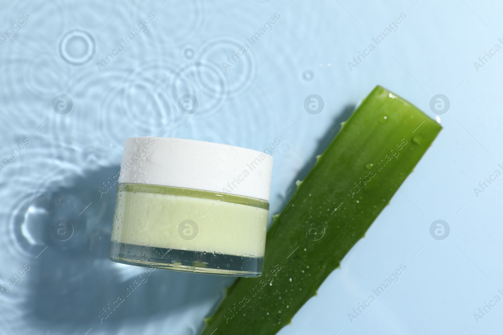 Photo of Jar of cosmetic product and aloe leaf in water on light blue background, flat lay