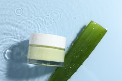 Photo of Jar of cosmetic product and aloe leaf in water on light blue background, flat lay