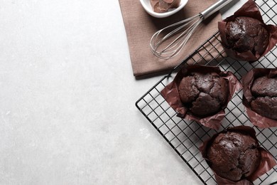Photo of Tasty chocolate muffins and whisk on grey table, flat lay. Space for text