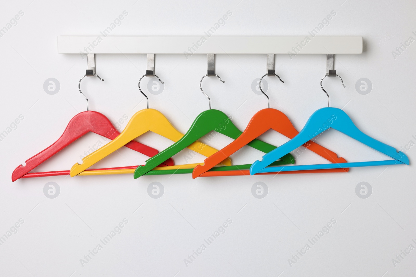 Photo of Rack with empty bright clothes hangers on white wall