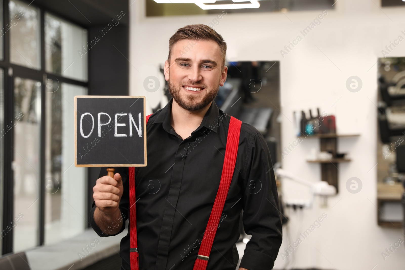 Photo of Young business owner holding OPEN sign in his barber shop