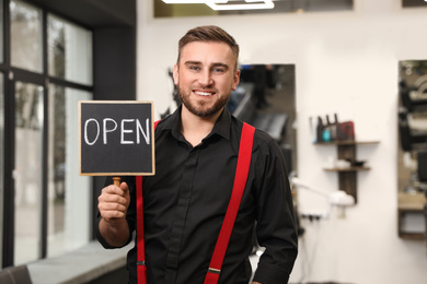 Photo of Young business owner holding OPEN sign in his barber shop