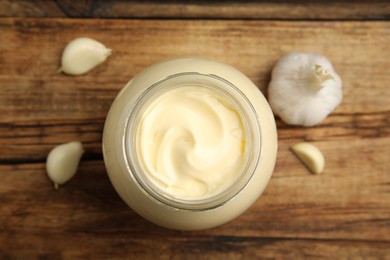 Jar of delicious mayonnaise and fresh garlic on wooden table, flat lay