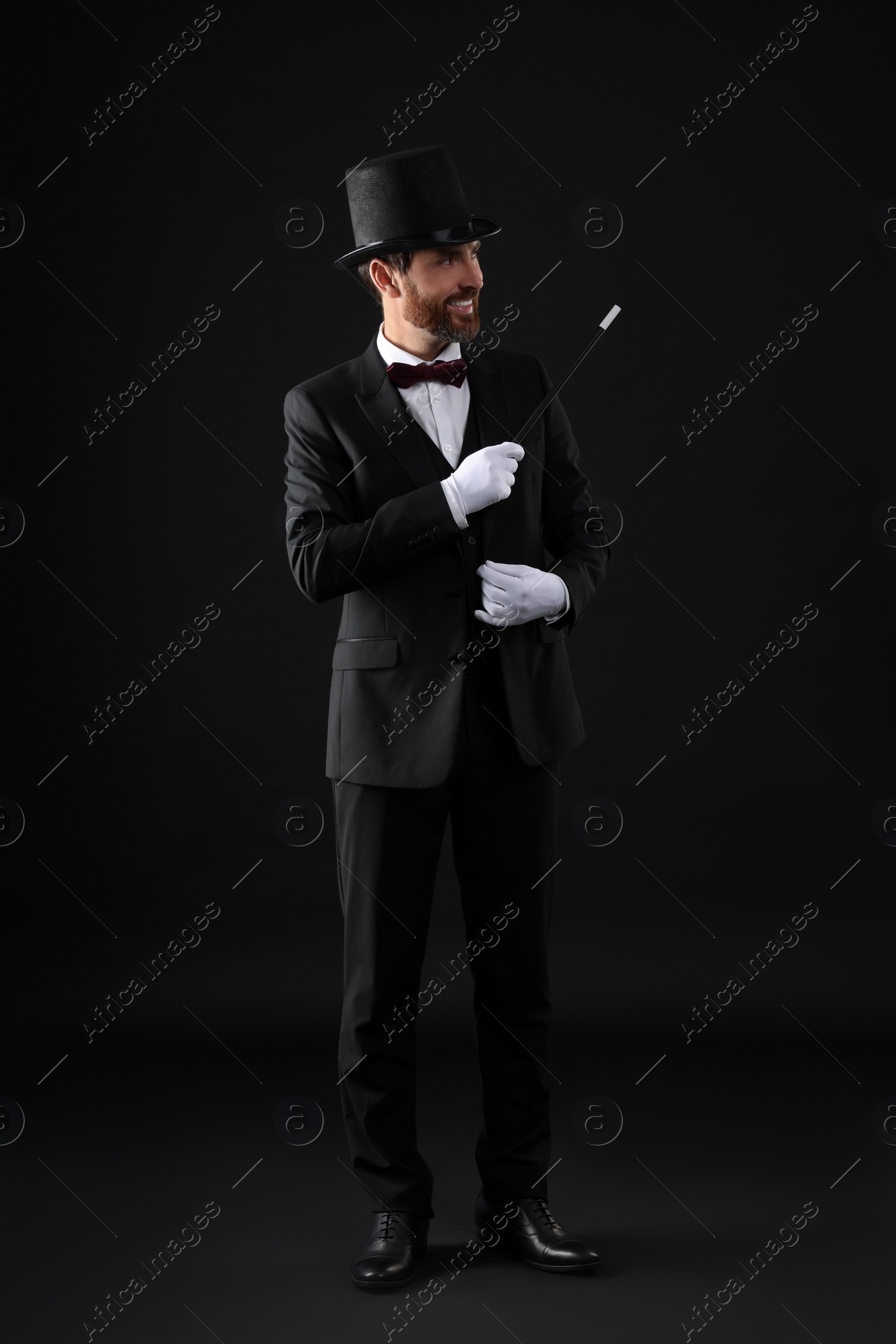 Photo of Happy magician holding wand on black background