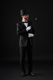 Happy magician holding wand on black background