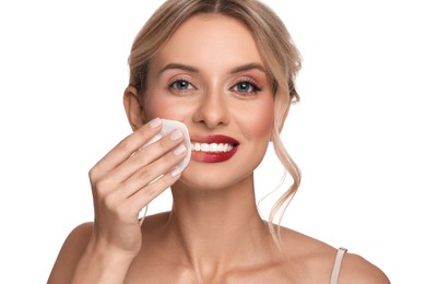 Smiling woman removing makeup with cotton pad on white background