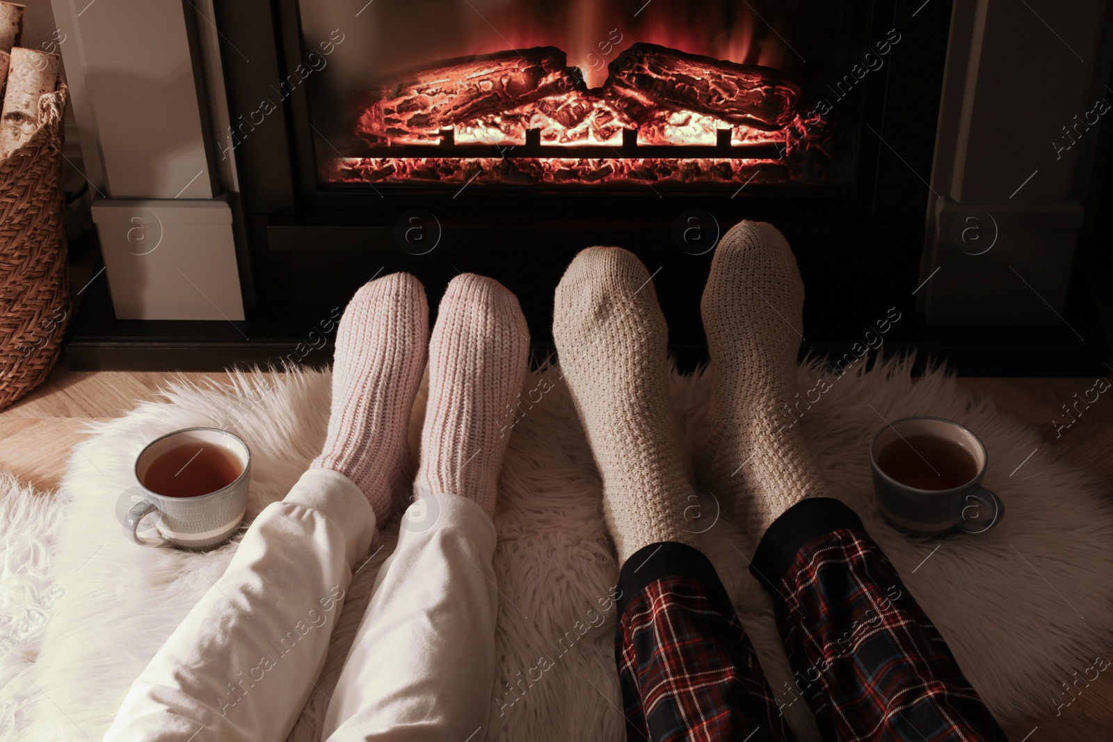 Photo of Couple in knitted socks near fireplace at home, closeup of legs