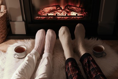 Photo of Couple in knitted socks near fireplace at home, closeup of legs