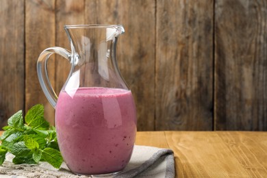 Photo of Glass jug of blackberry smoothie and mint on wooden table, space for text