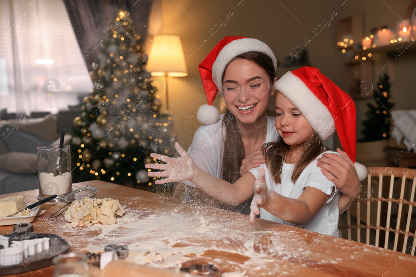 Photo of Mother with her cute little daughter having fun while making dough for Christmas cookies in kitchen