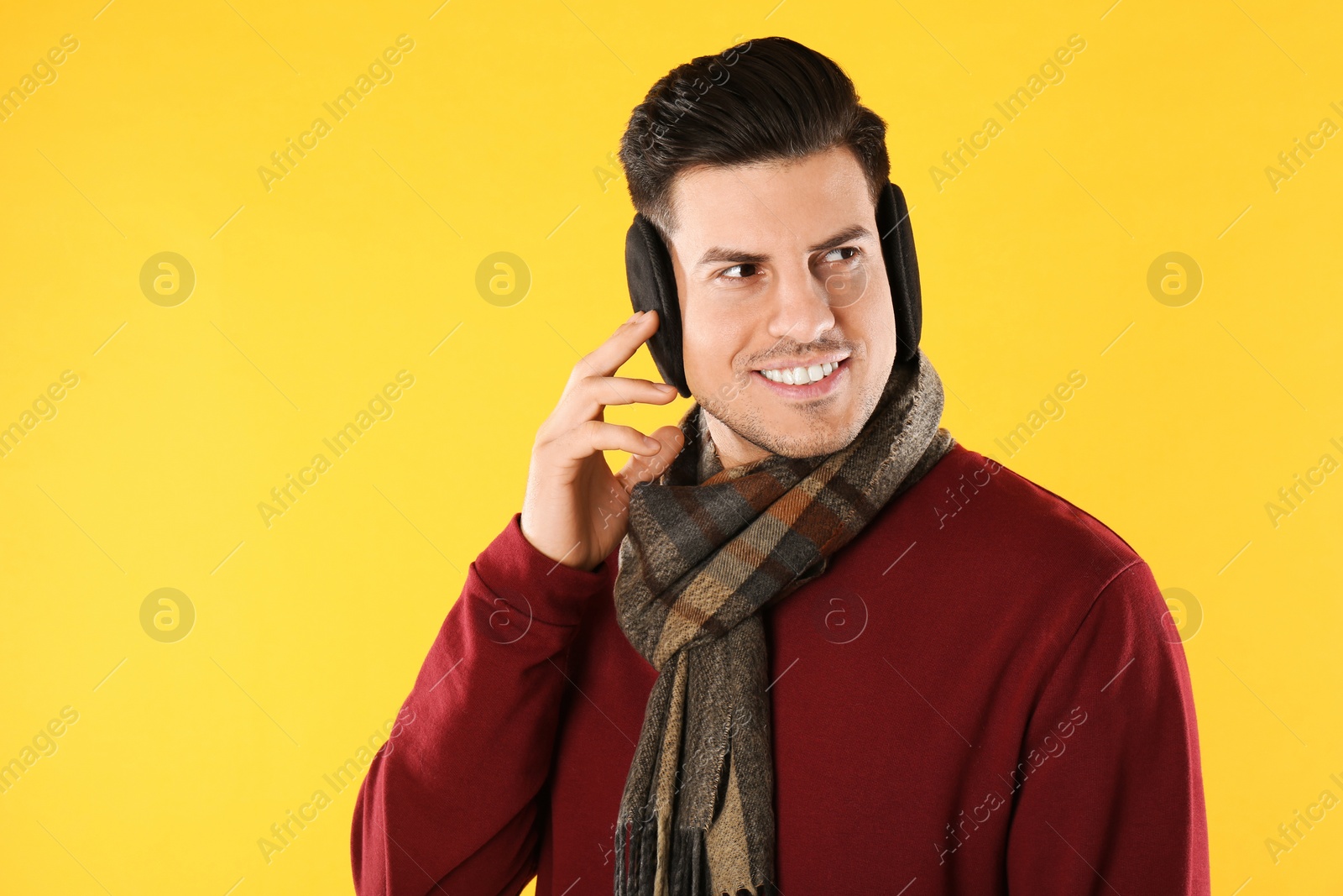 Photo of Man wearing stylish earmuffs and scarf on yellow background