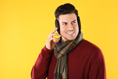 Photo of Man wearing stylish earmuffs and scarf on yellow background