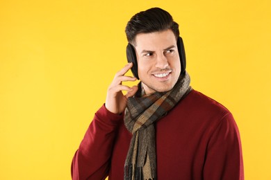 Man wearing stylish earmuffs and scarf on yellow background