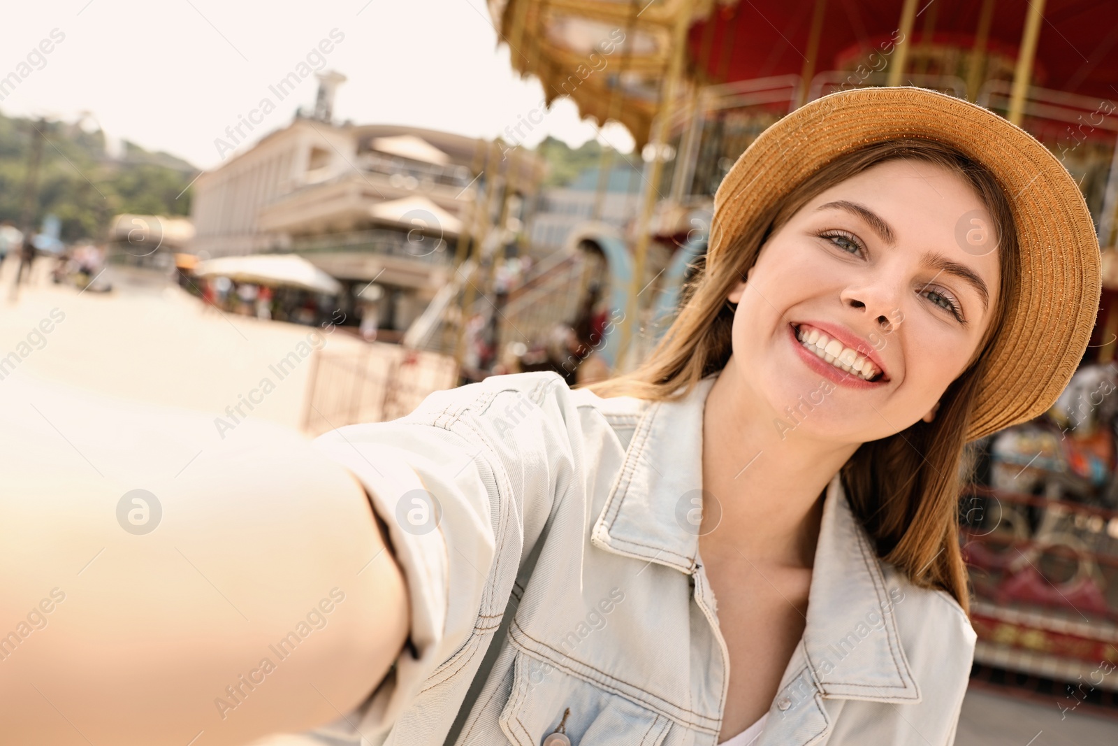 Photo of Young pretty woman taking selfie near carousel in amusement park