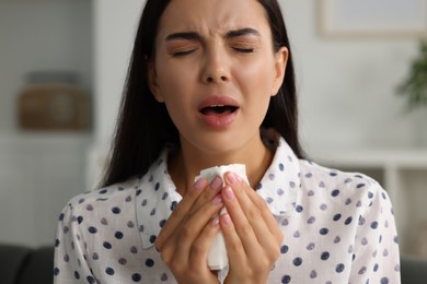 Photo of Suffering from allergy. Young woman with tissue sneezing indoors