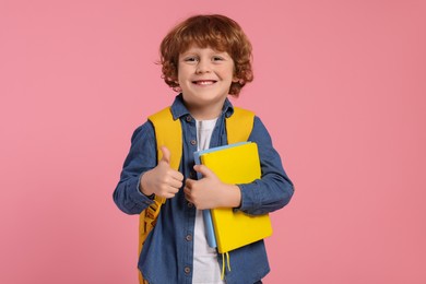 Photo of Happy schoolboy with backpack and books showing thumb up gesture on pink background