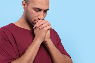 Photo of African American man with clasped hands praying to God on light blue background, closeup. Space for text