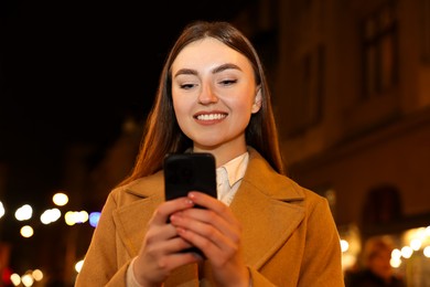 Photo of Smiling woman using smartphone on night city street