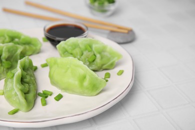 Photo of Delicious green dumplings (gyozas) and soy sauce on white tiled table, closeup. Space for text