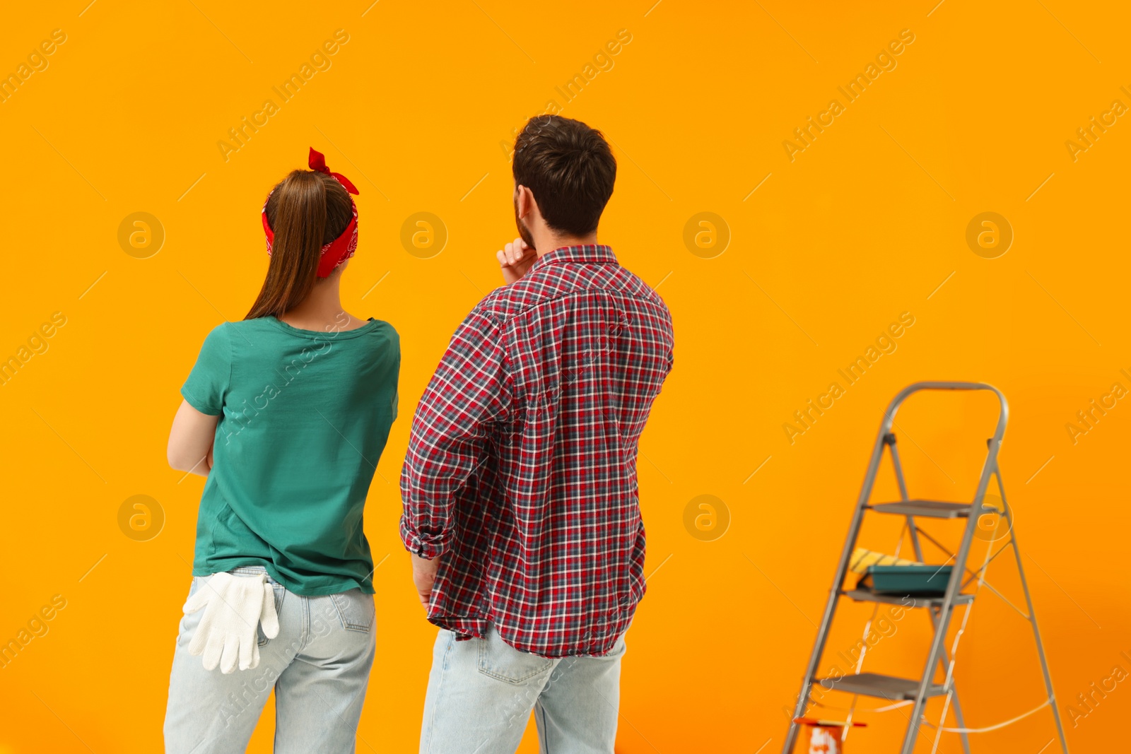 Photo of Designers looking at freshly painted orange wall, back view