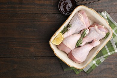 Photo of Marinade, raw chicken drumsticks, rosemary and lemon on wooden table, flat lay. Space for text