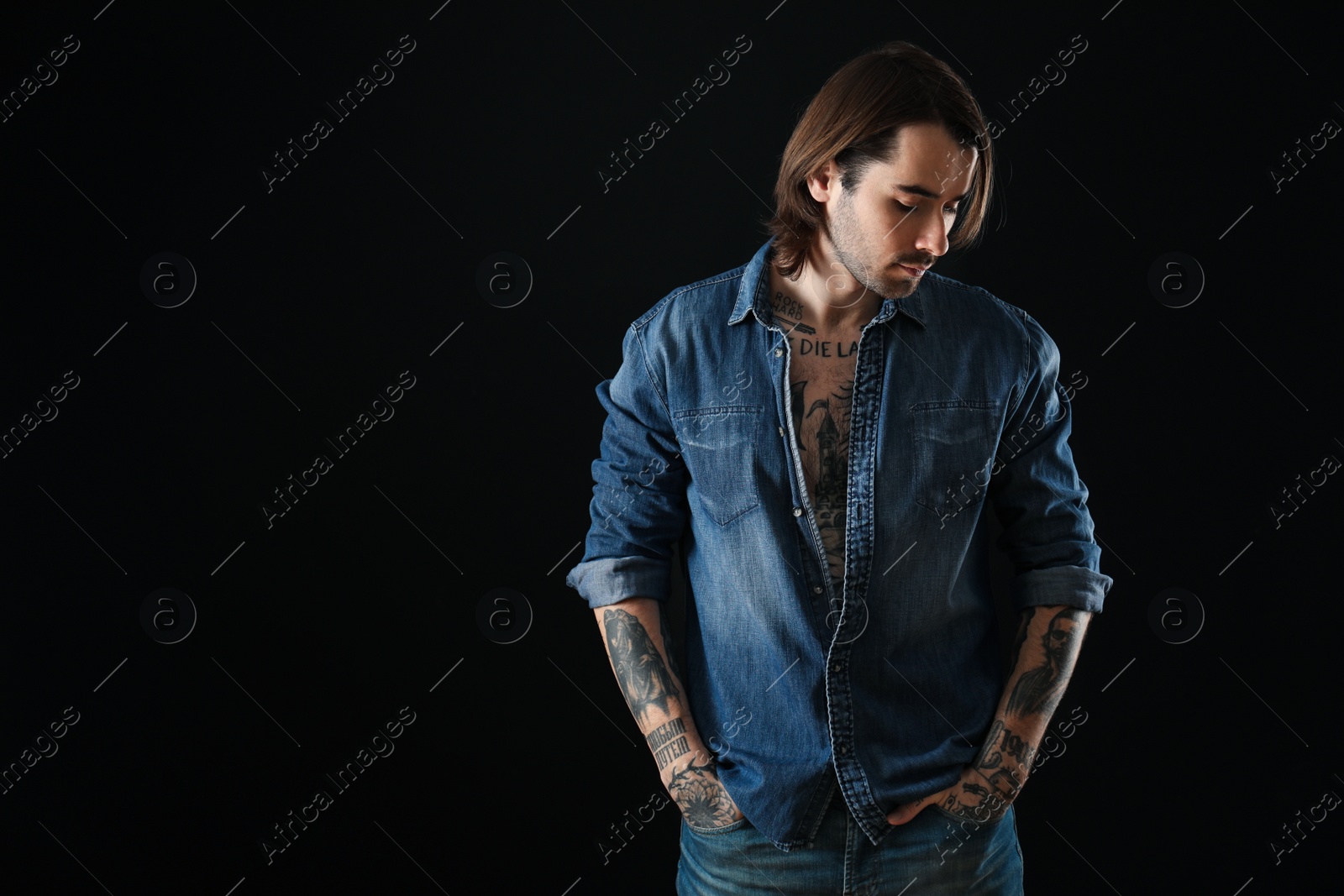 Photo of Young man with tattoos on body against black background. Space for text