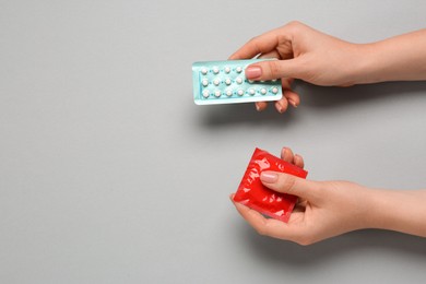 Photo of Woman holding condom and contraceptive pills on gray background, top view with space for text. Choosing birth control method