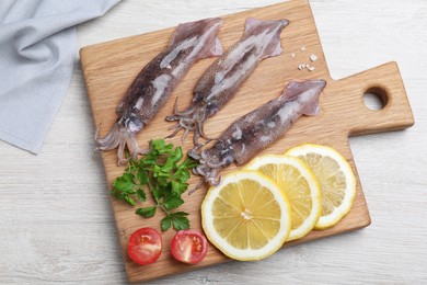 Photo of Fresh raw squids with lemon, parsley and tomato on white wooden table, top view