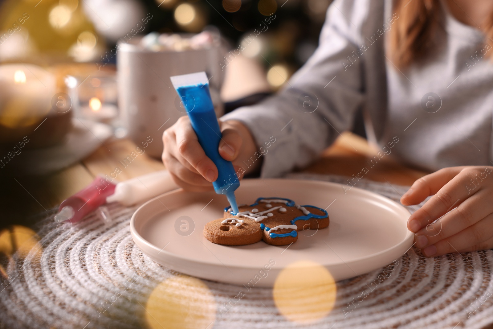 Photo of Little child decorating Christmas cookie at table, closeup