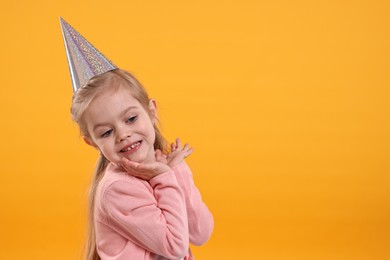 Photo of Birthday celebration. Cute little girl in party hat on orange background, space for text
