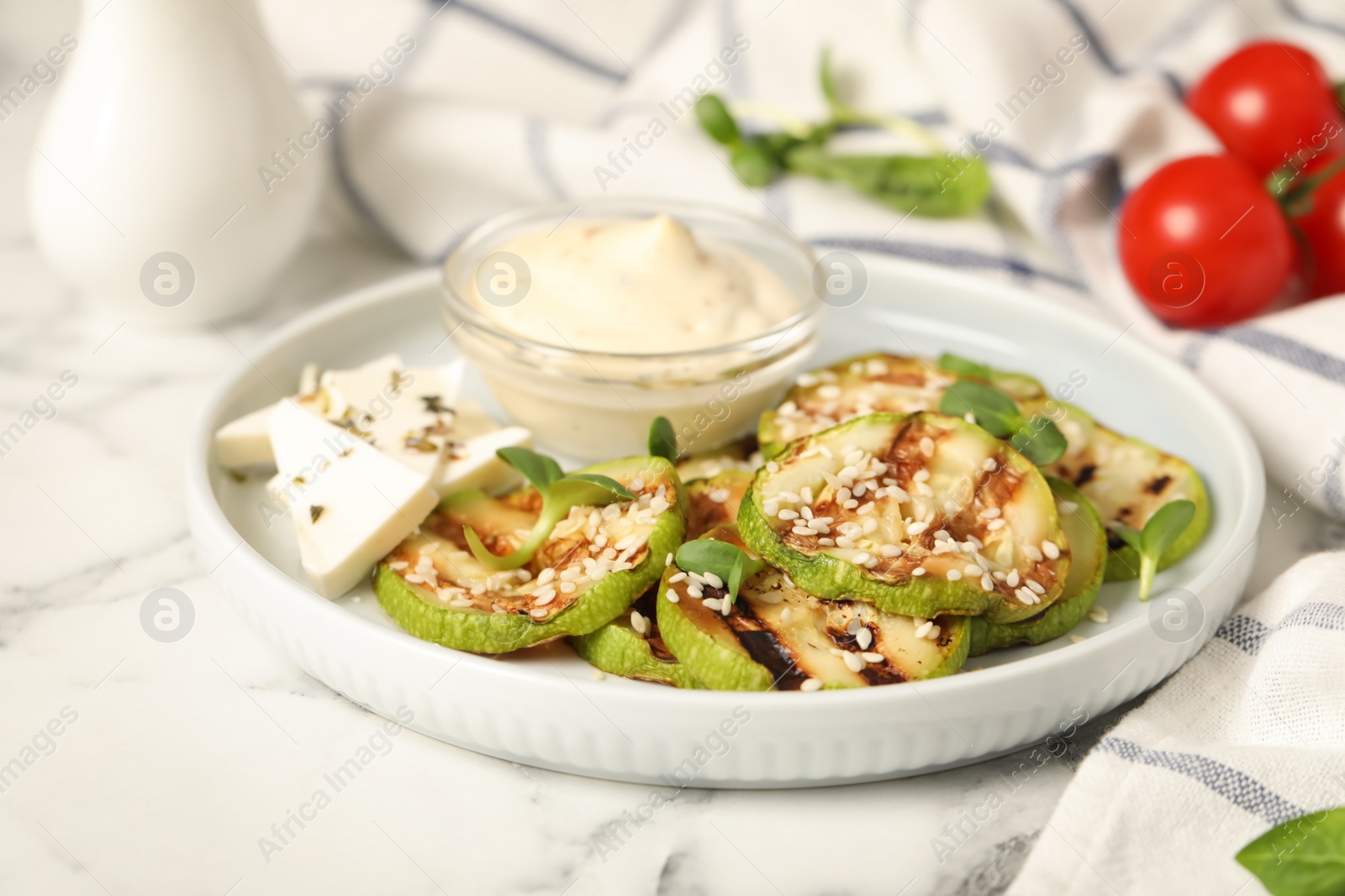 Photo of Delicious grilled zucchini slices served with sauce and cheese on white marble table, closeup