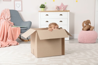 Photo of Cute little girl playing with cardboard box at home