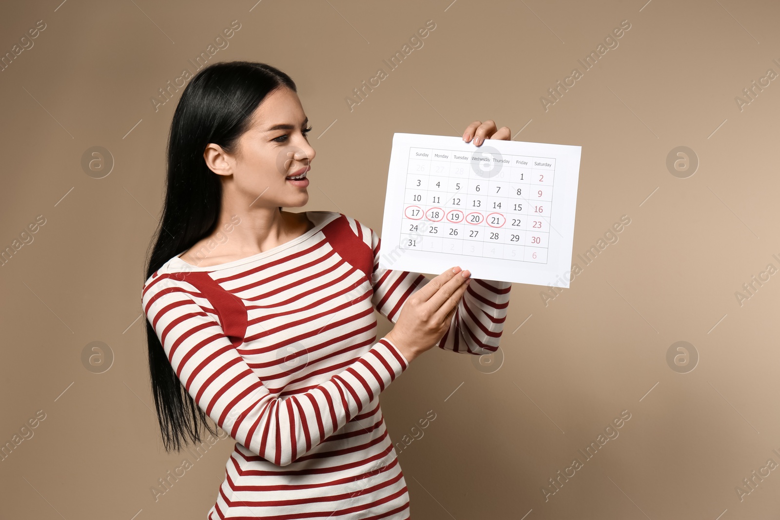 Photo of Young woman holding calendar with marked menstrual cycle days on beige background