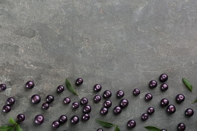 Photo of Fresh acai berries and green leaves on grey table, flat lay. Space for text